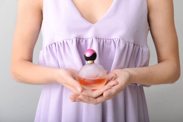 Женщина с бутылкой духов на сером фоне, крупным планом
