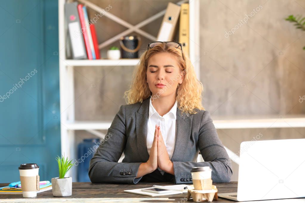 Beautiful businesswoman meditating at table in office