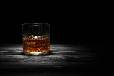Glass of whisky with ice on wooden table against black background clipart