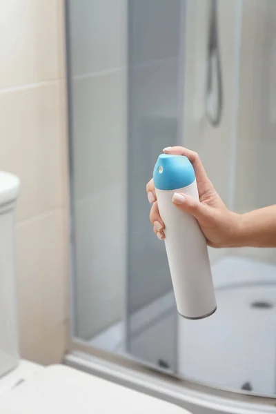 Woman holding spray air freshener in bathroom