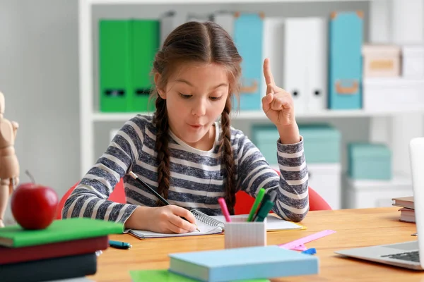 Cute girl with raised index finger doing homework in classroom