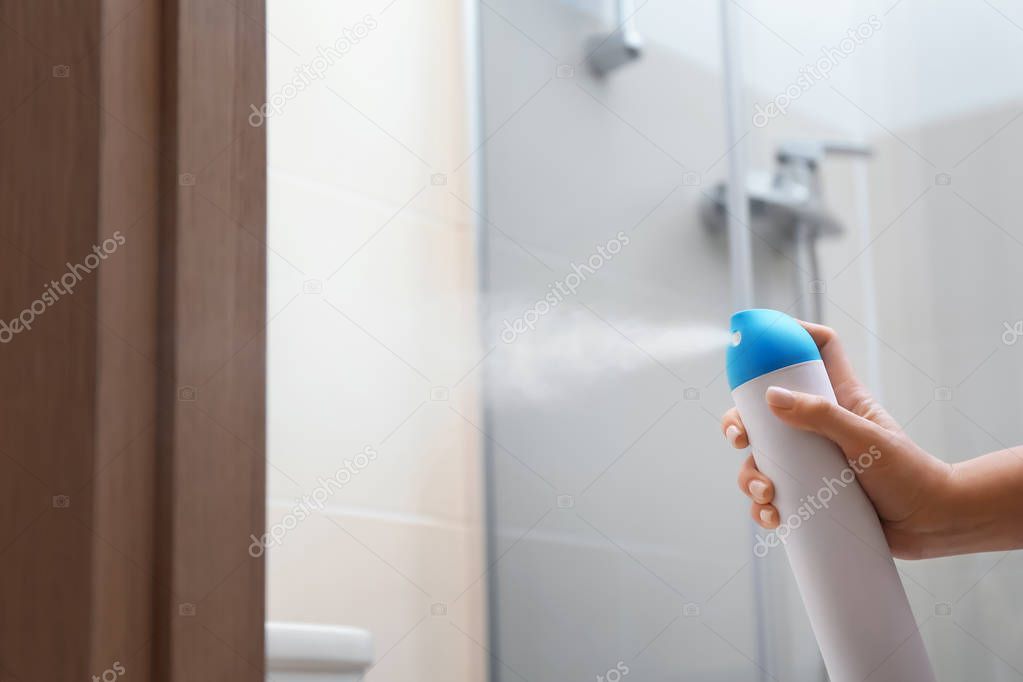 Woman spraying air freshener in bathroom