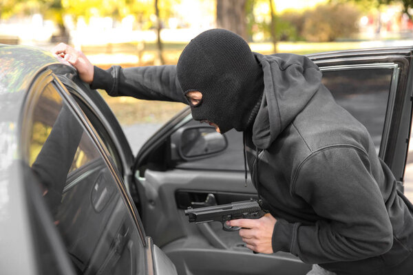 Male thief with gun near open car outdoors