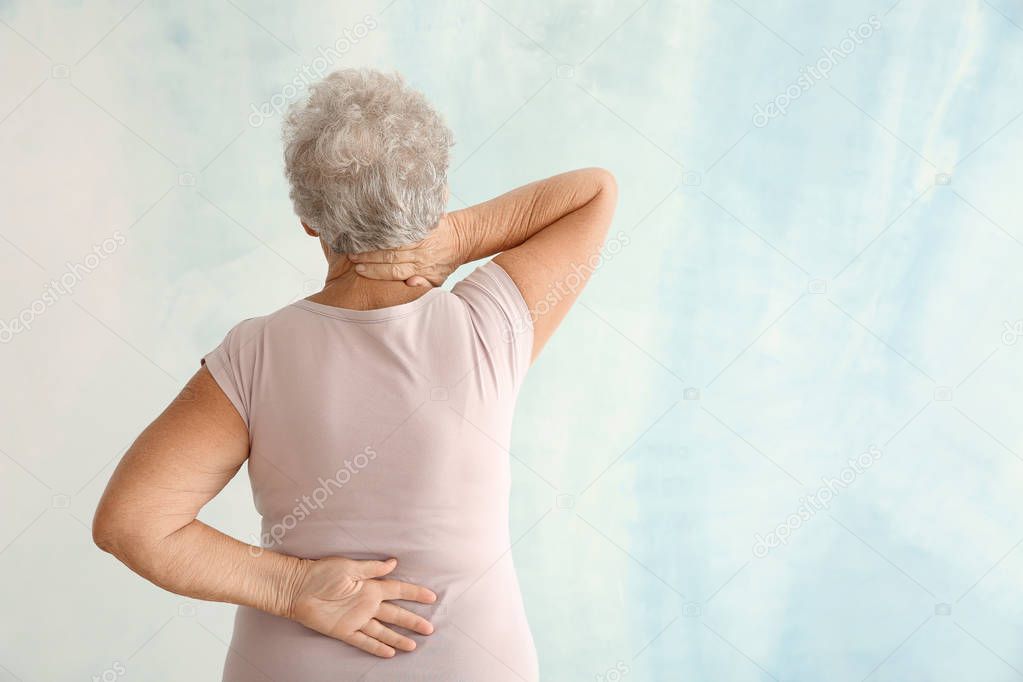 Senior woman suffering from back pain on light background