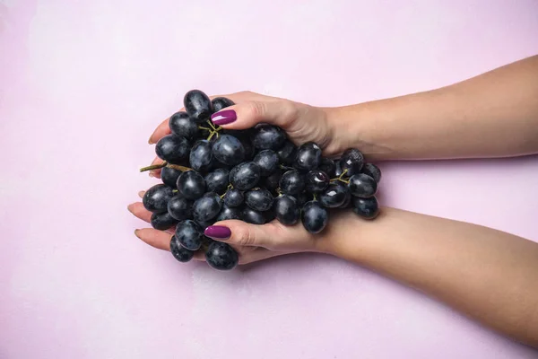 Female hands with ripe tasty grapes on color background