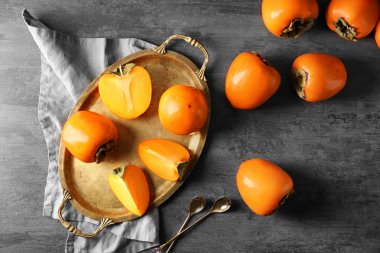 Tray with ripe persimmons on grey background, top view clipart