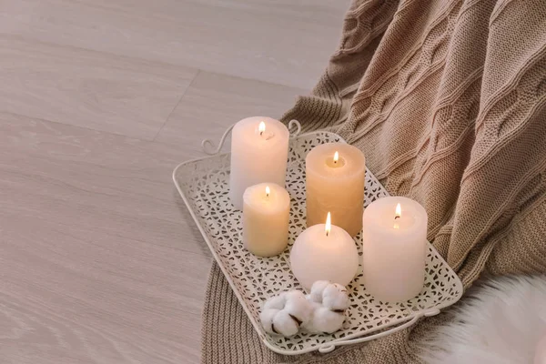 Tray with burning candles and cotton flowers on floor