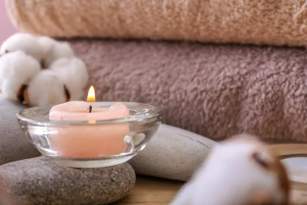 Burning candle, spa stones and cotton flowers on table, closeup