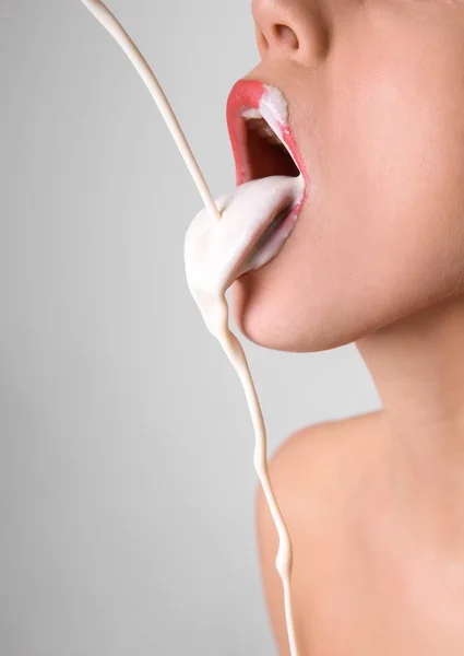 White liquid dripping into woman\'s mouth on light background. Erotic concept