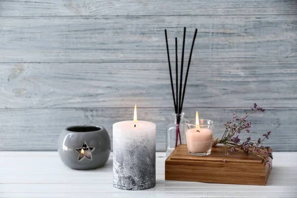 Beautiful composition with burning candles on table near wooden wall