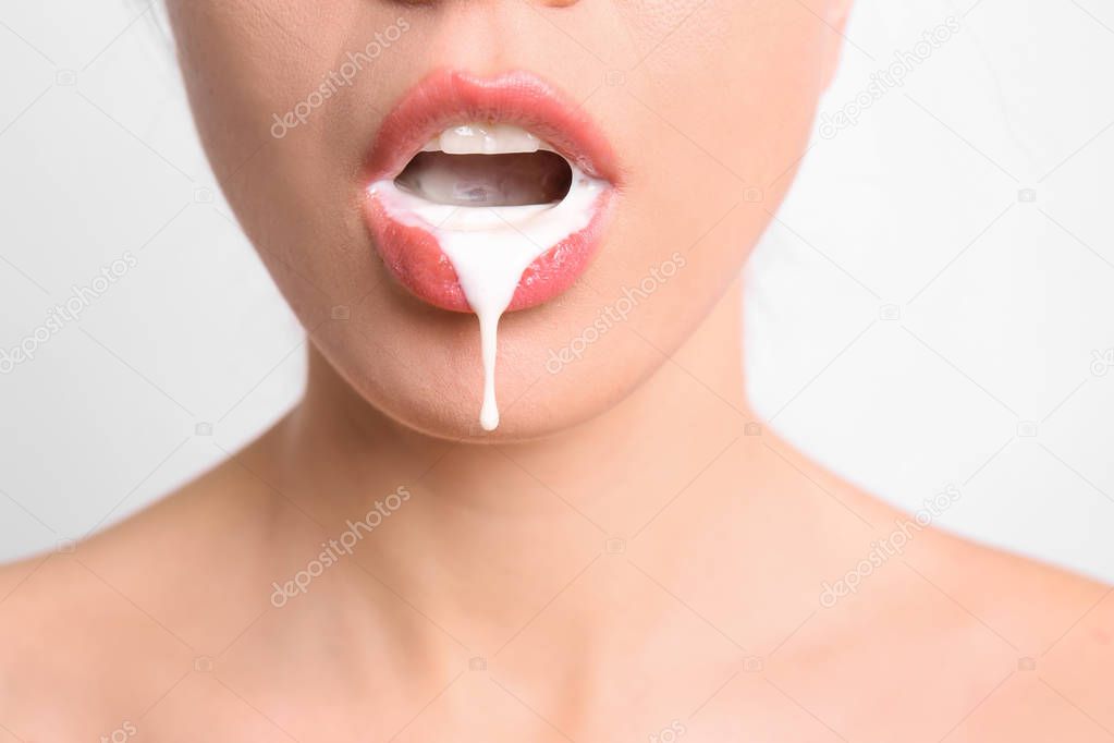 Young woman with white liquid dripping from her mouth on light background. Erotic concept