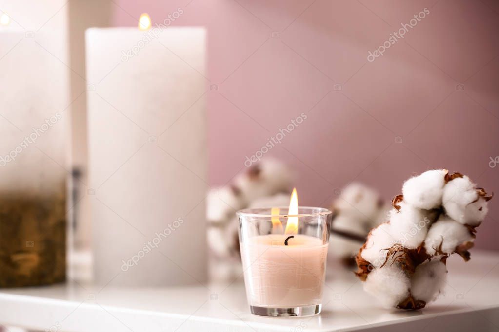 Burning candles and cotton flowers on shelf