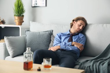 Sarhoş adam şişe ve bardak viski ile tablo yakınındaki kanepede uyuyor. Alkolizm kavramı