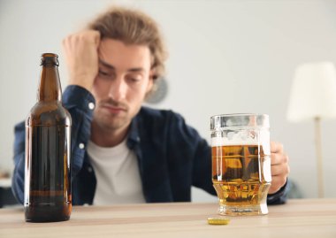 Depresif genç adam evde bira içiyor. Alkolizm kavramı