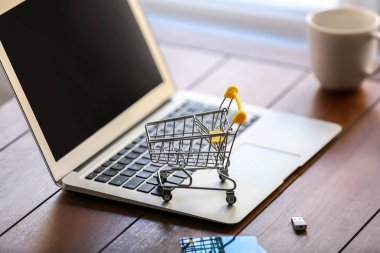 Dizüstü bilgisayar ve kredi kartları ahşap masa üzerinde küçük el arabası. Online alışveriş