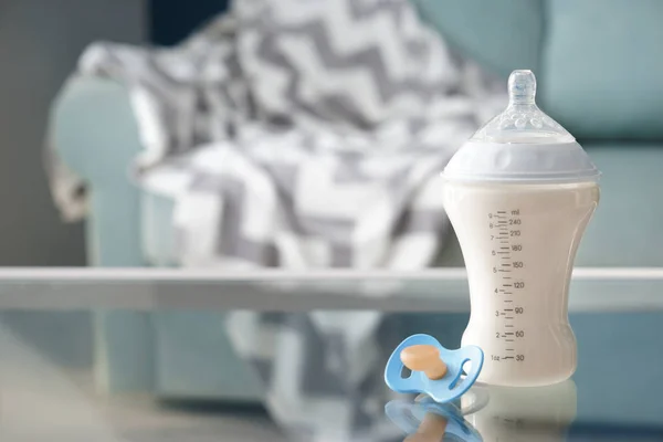 Feeding bottle of baby formula with pacifier on glass table