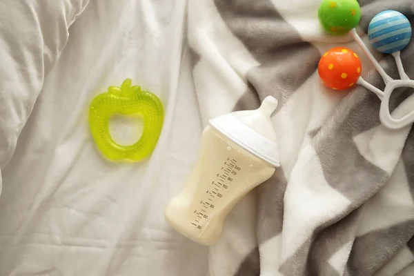 Feeding bottle of baby formula with toys on bed