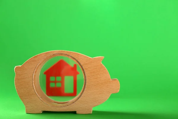 Wooden piggy bank with house model on color background