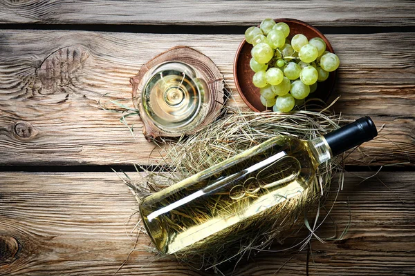 Glass and bottle of white wine with fresh grapes on wooden table