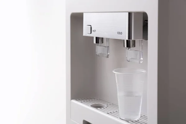 Modern water cooler with plastic cup on white background