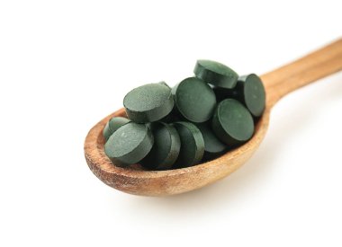 Spirulina tablet beyaz zemin üzerine kaşıkla