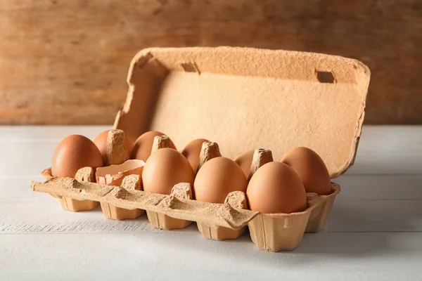 Cracked and whole chicken eggs in carton box on white table