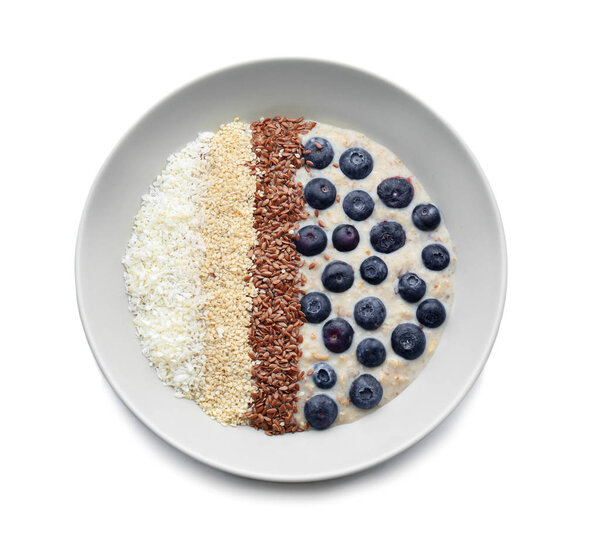 Plate with tasty oatmeal, sesame seeds and blueberries on white background