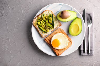 Kızarmış ekmek, avokado ve gri masada kızarmış yumurta ile plaka