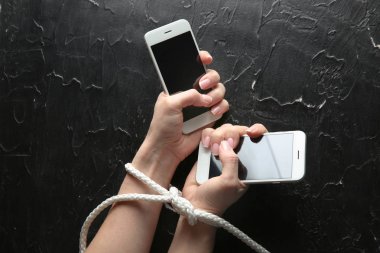 Kadın bağlı elleri ve cep telefonlarında koyu arka plan ile. Bağımlılık kavramı