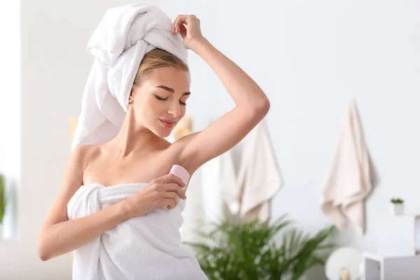 Beautiful young woman with deodorant in bathroom