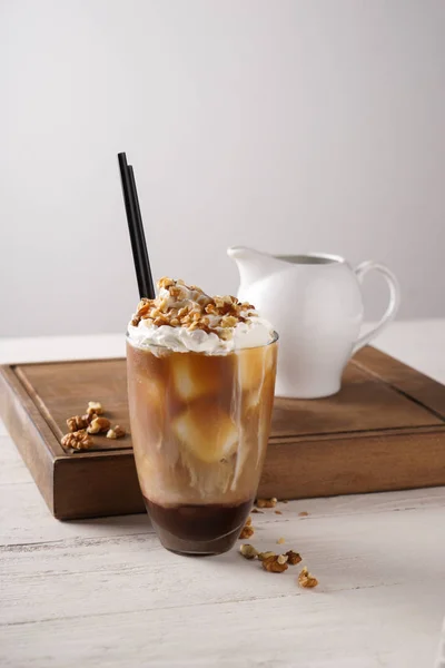 Glass of tasty cold coffee with walnuts on white wooden table