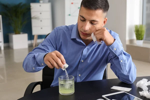 Young man ill with flu taking medicine in office