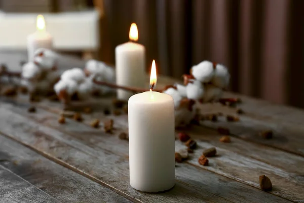 Burning candles with cotton flowers on wooden table