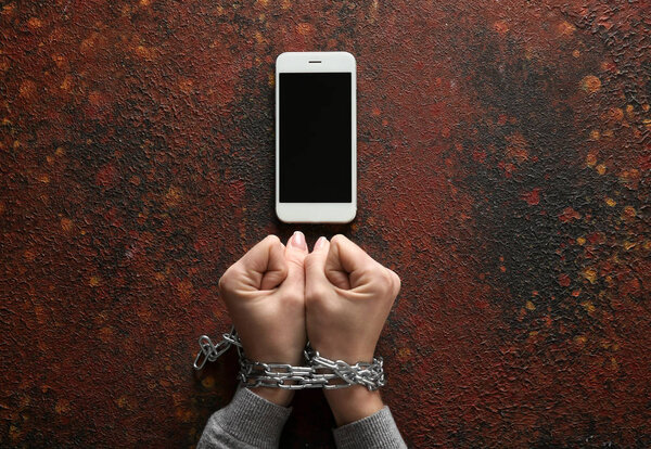 Женщина с прикованными руками и мобильным телефоном на цветном фоне. Концепция зависимости
