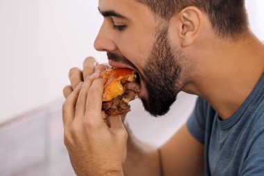 Lezzetli burger yiyen genç adam, yakın plan.