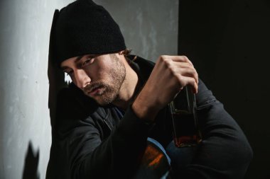 Karanlık odada viski şişesi olan depresif genç adam. Alkolizm kavramı