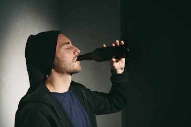 Depresif genç adam karanlık odada bira içiyor. Alkolizm kavramı