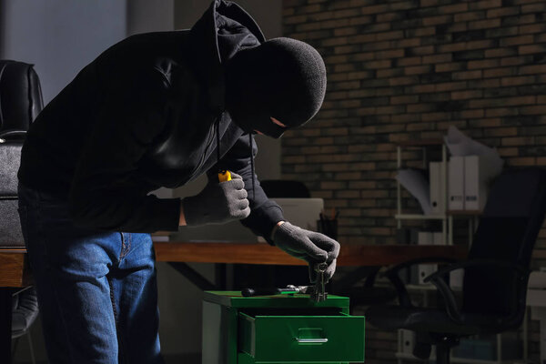 Вор-мужчина с фонариком в офисе
