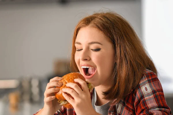 家でおいしいハンバーガーを食べる若い女性 — ストック写真