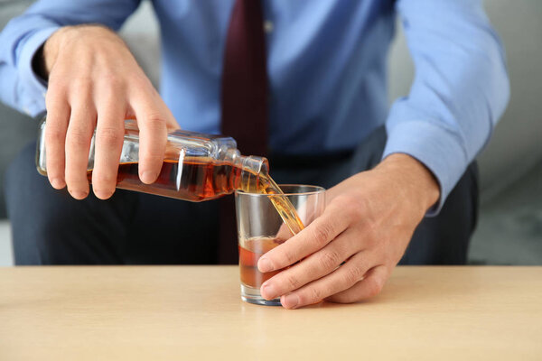 Man pouring alcohol from bottle into glass at table, closeup. Alcoholism concept