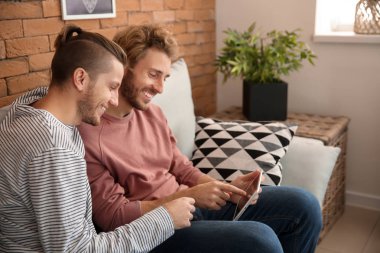 Mutlu genç gay çift ile tablet Pc evde koltukta oturan