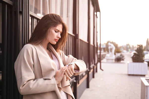 Young woman looking at watch while waiting for her boyfriend outdoors