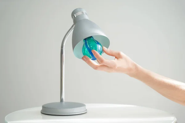 Woman changing light bulb in lamp on grey background