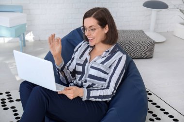 Ofiste beanbag sandalye üzerinde oturan dizüstü bilgisayar ile genç iş kadını