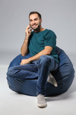 Cep telefonu gri bir arka plana dayanır beanbag sandalye üzerinde oturan genç adam