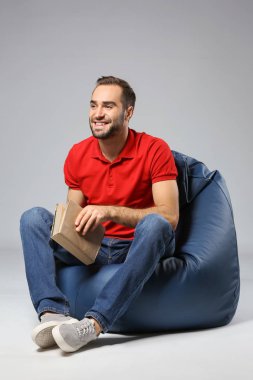 Kitap beanbag sandalye gri arka plan üzerinde oturan genç adam