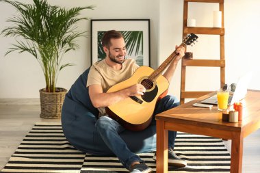 Evde beanbag sandalye üzerinde oturan gitar ile genç adam