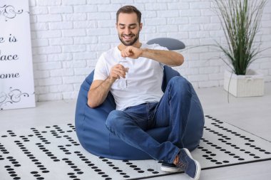 Şişe suyu evde beanbag sandalye üzerinde oturan genç adam