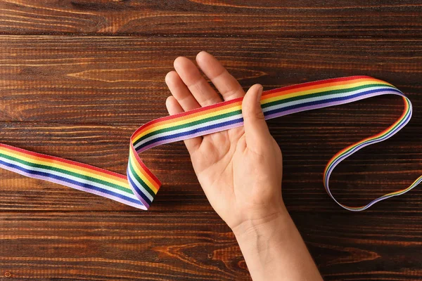 Woman holding rainbow ribbon of LGBT on wooden background