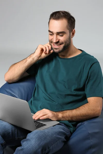 Молодий Чоловік Ноутбуком Сидить Кріслі Мішків Сірому Фоні — стокове фото